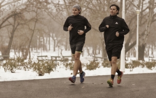 Zwei Männer joggen nebeneinander an einem verschneiten Park.