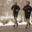 Zwei Männer joggen nebeneinander an einem verschneiten Park.