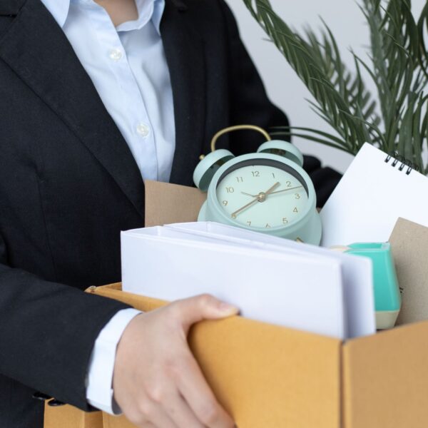 Eine Person, deren Gesicht man nicht sieht, trägt einen Karton mit Büroartikeln.