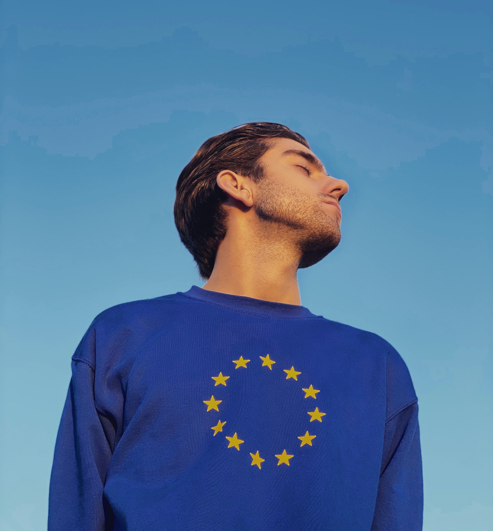 Ein Mann mit einem blauen Pullover, auf dem das Zeichen der EU (ein Kreis aus Sternen) abgebildet ist.